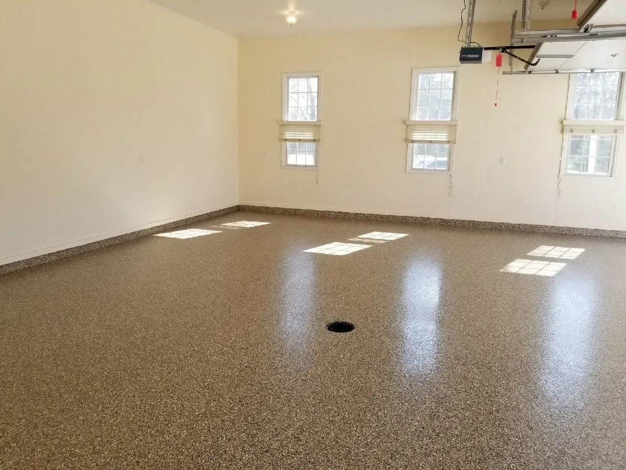 Empty garage with speckled epoxy floor, white walls, windows, and a basketball hoop
