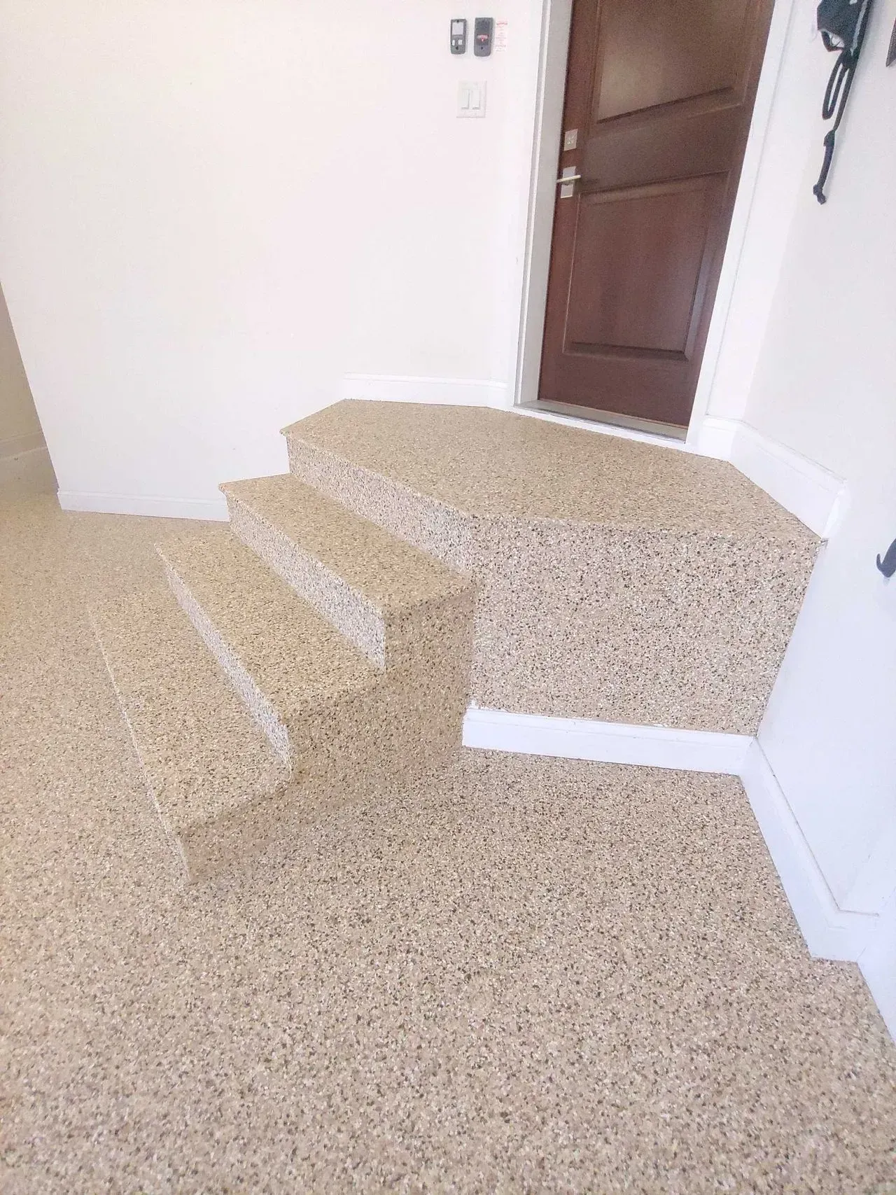 Carpeted stairs leading to a brown door in a white hallway.