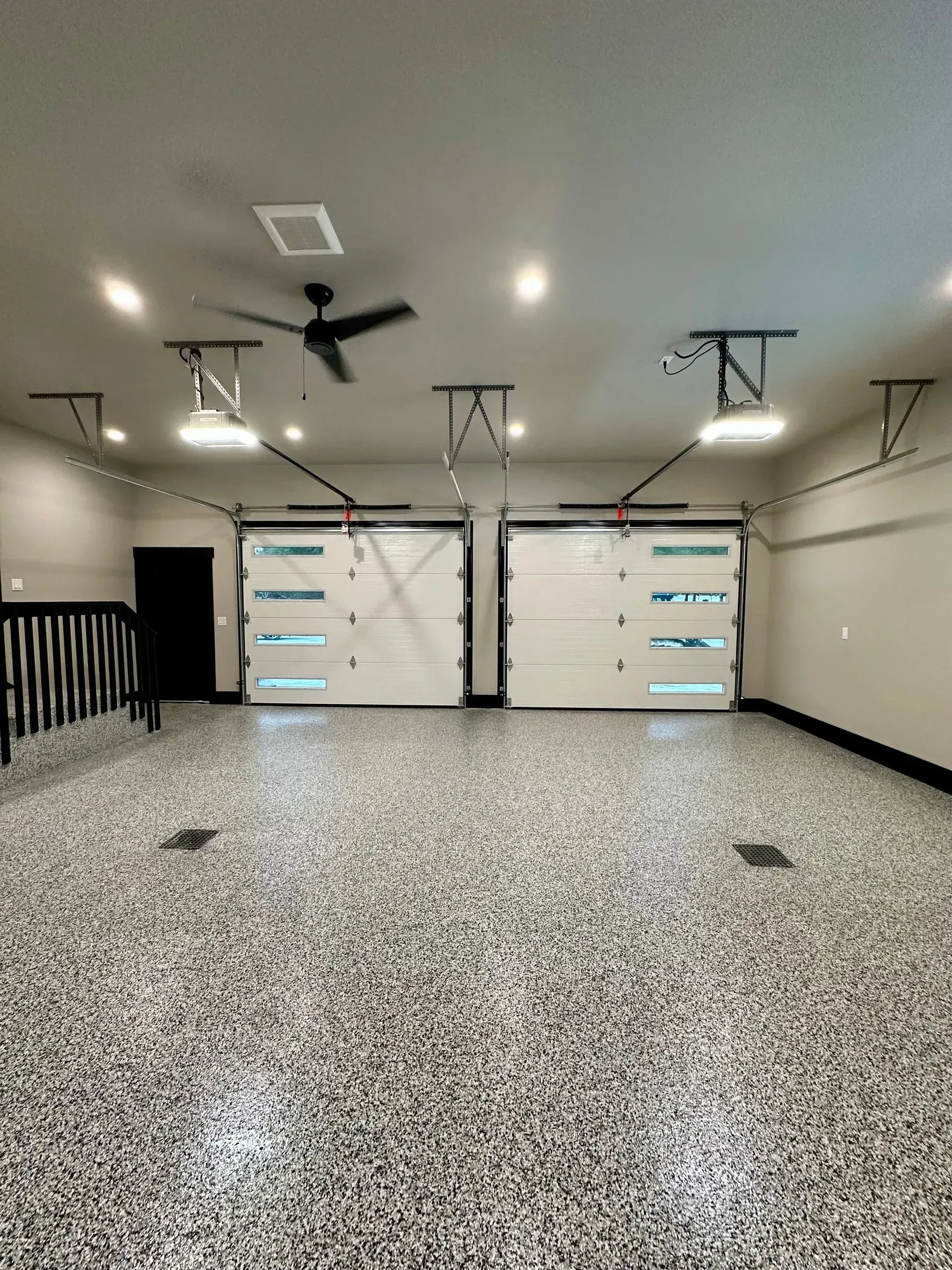 Spacious garage with speckled epoxy floor, double doors, ceiling lights, and a ceiling fan.