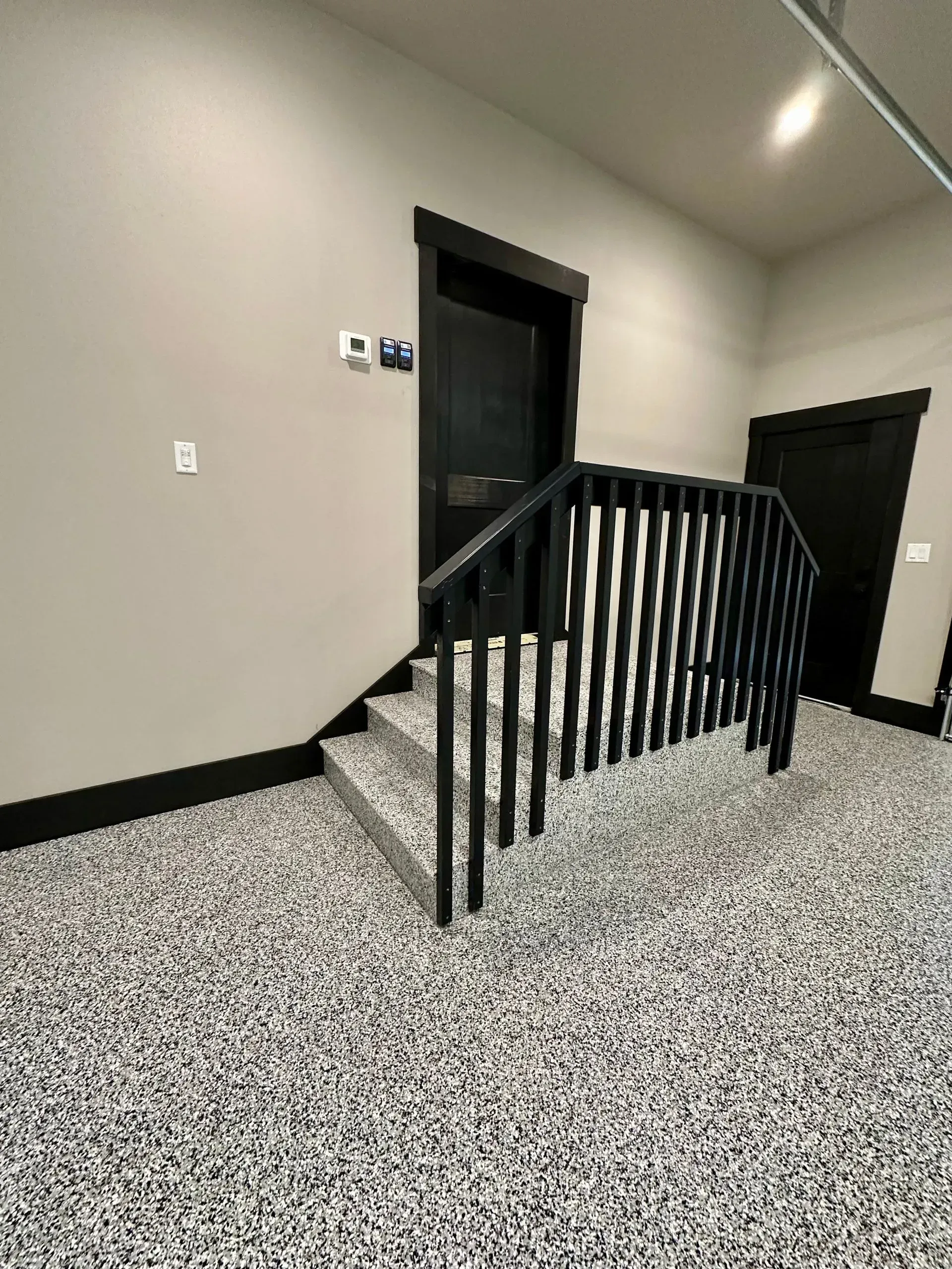 Indoor staircase with black railing, dark doors, and light gray walls in a modern hallway.
