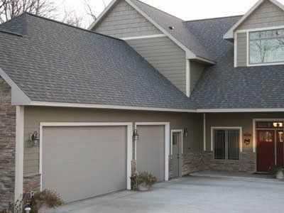 Suburban house exterior with gray roof, two-car garage, and front entrance with stone siding