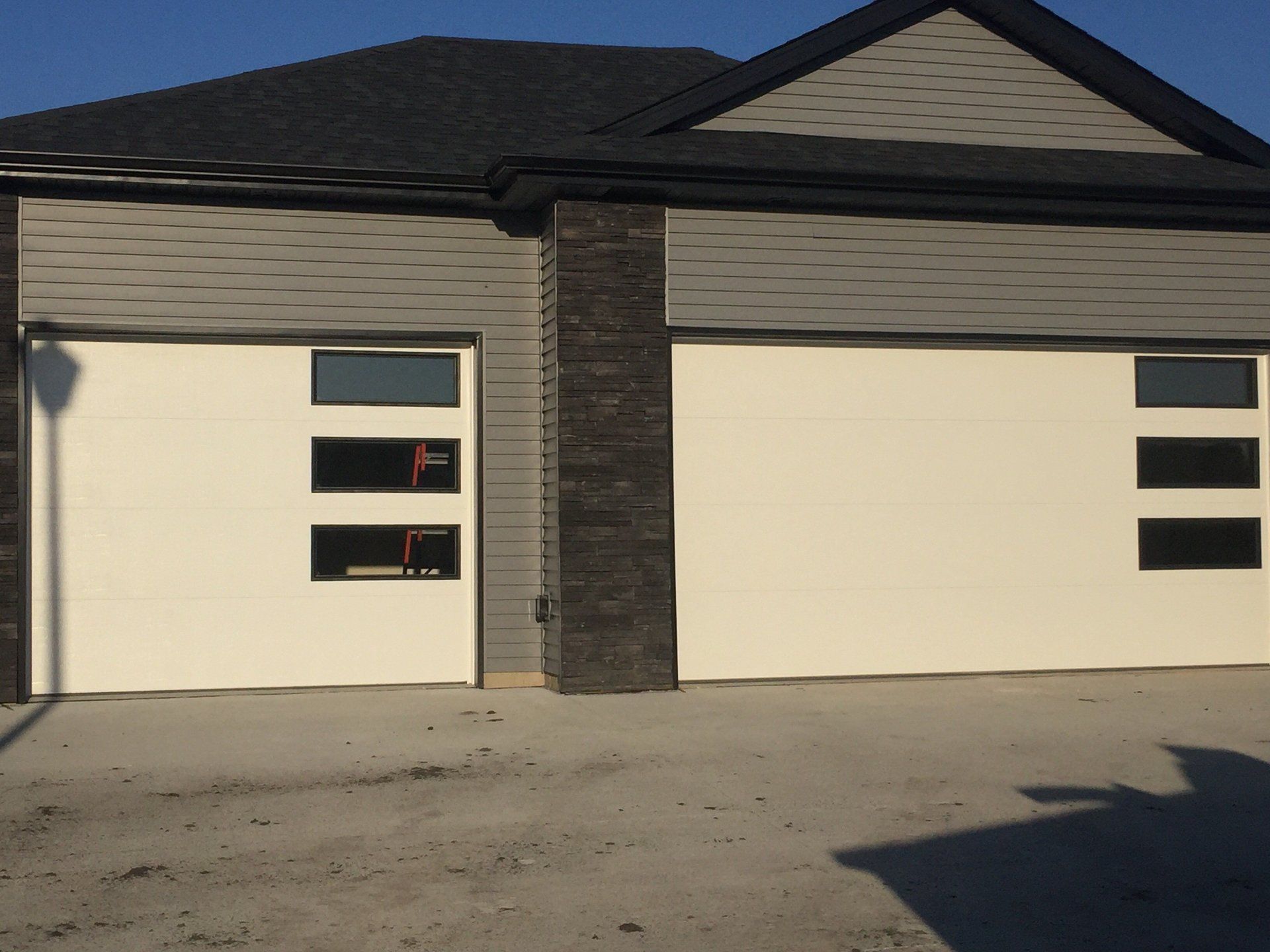Two cream garage doors on a modern house with dark trim and a paved driveway