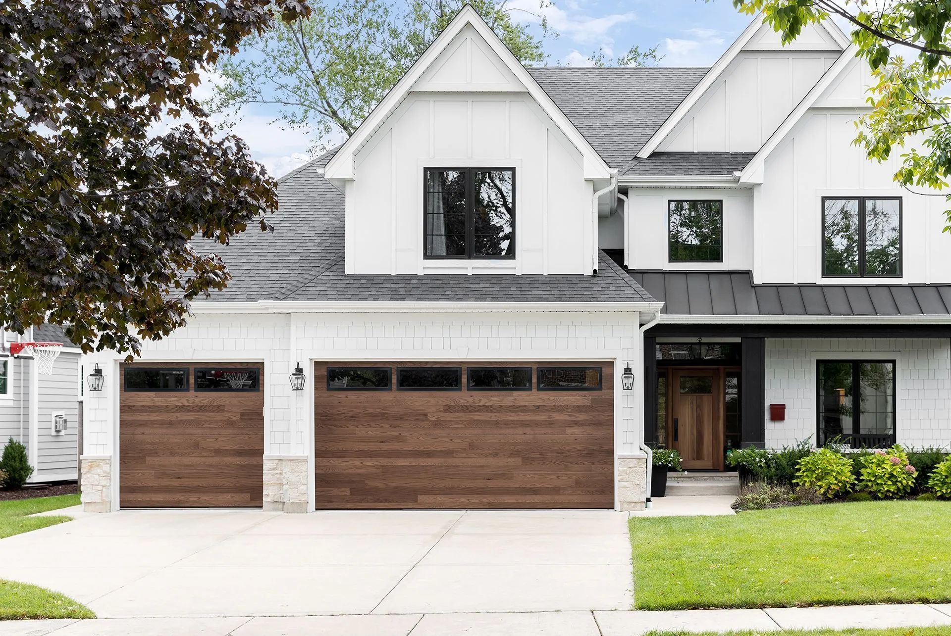 Modern two-story suburban house with white siding, gray roof, and three-car wooden garage doors