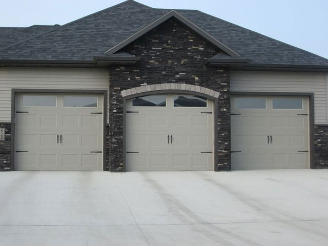 Three-car garage with beige doors and dark stone facade, viewed from the driveway.