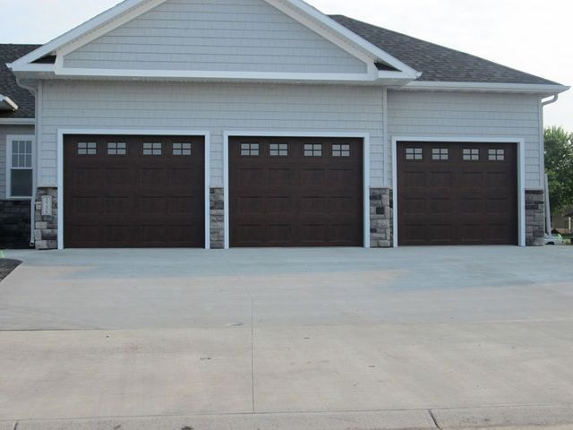 Three-car garage with white siding and dark brown doors, viewed from a concrete driveway.