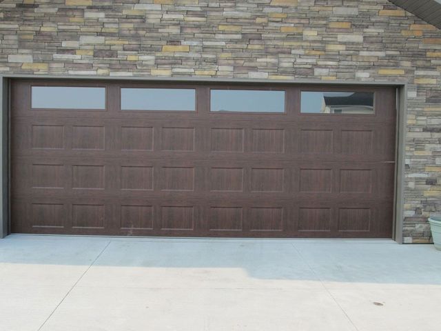 Brown garage door with small windows set in a stone house exterior.