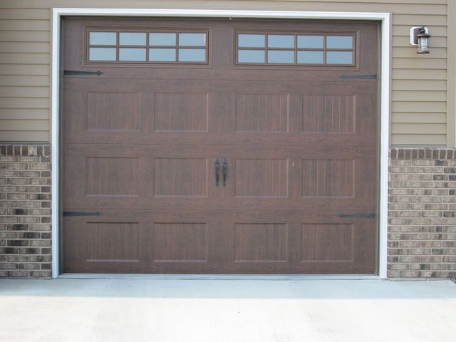 Closed brown garage door with four small windows, set in a beige house exterior.