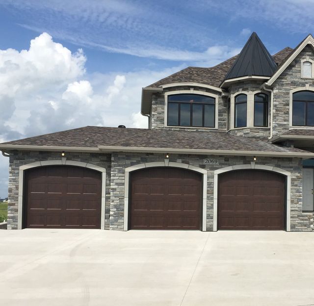 Stone suburban house with three brown garage doors and a clear blue sky