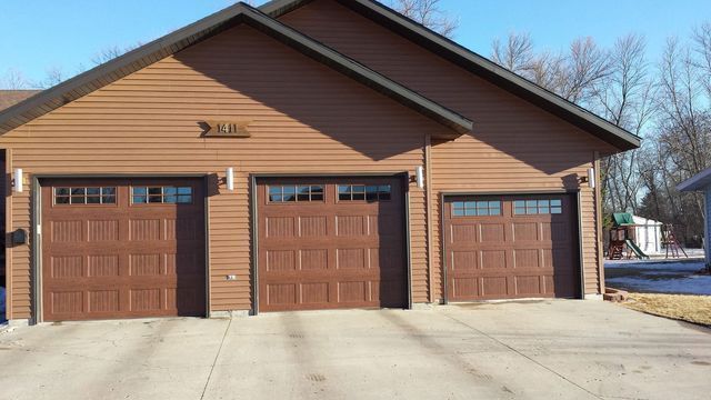Three-car brown garage with tan siding and concrete driveway on a clear day