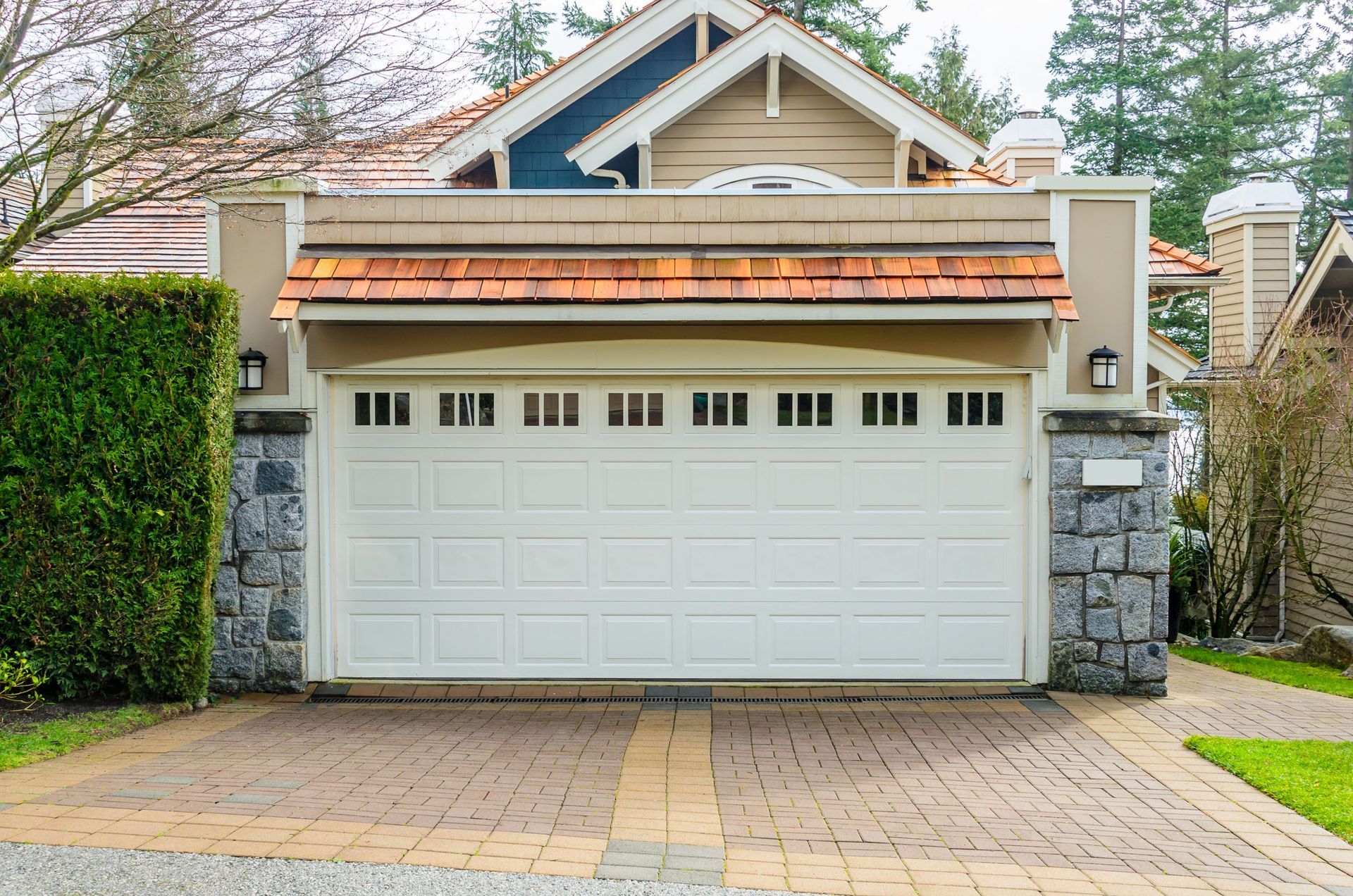 Front view of a two-car garage with white doors, stone pillars, and a brick driveway.