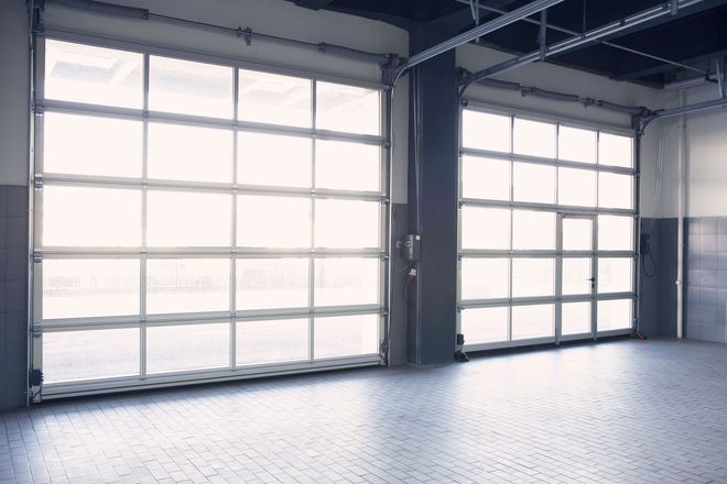 Empty industrial room with large frosted garage doors and bright light streaming in.