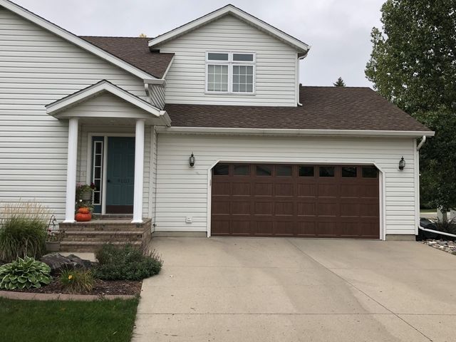 Suburban house exterior with white siding, brown garage door, and concrete driveway