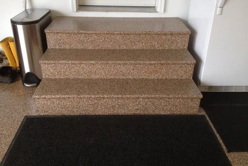 Empty gray speckled floor with a small black staircase against a white wall