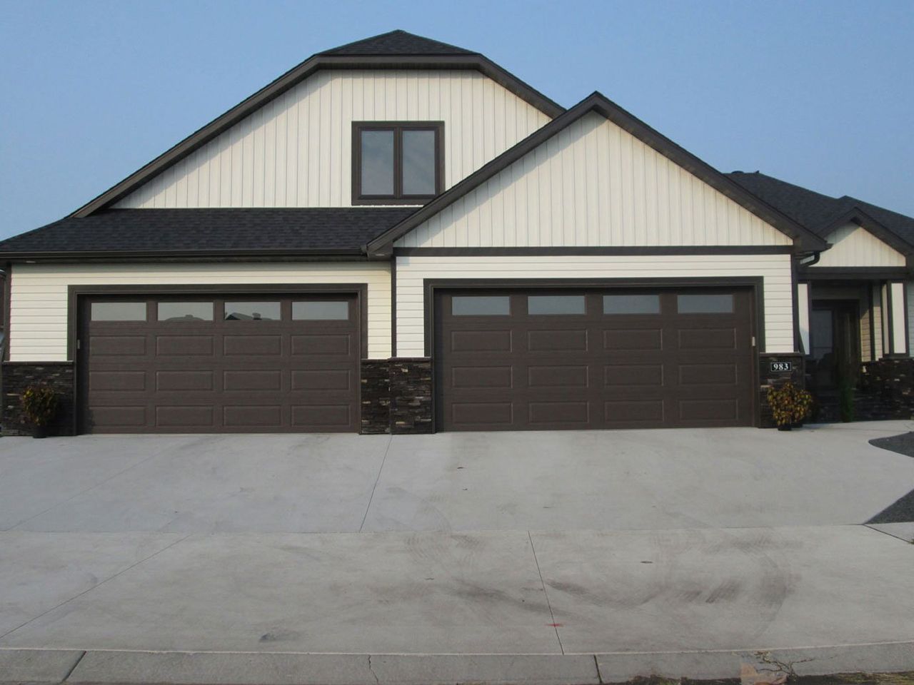 Modern beige house with a dark roof and two brown garage doors on a concrete driveway