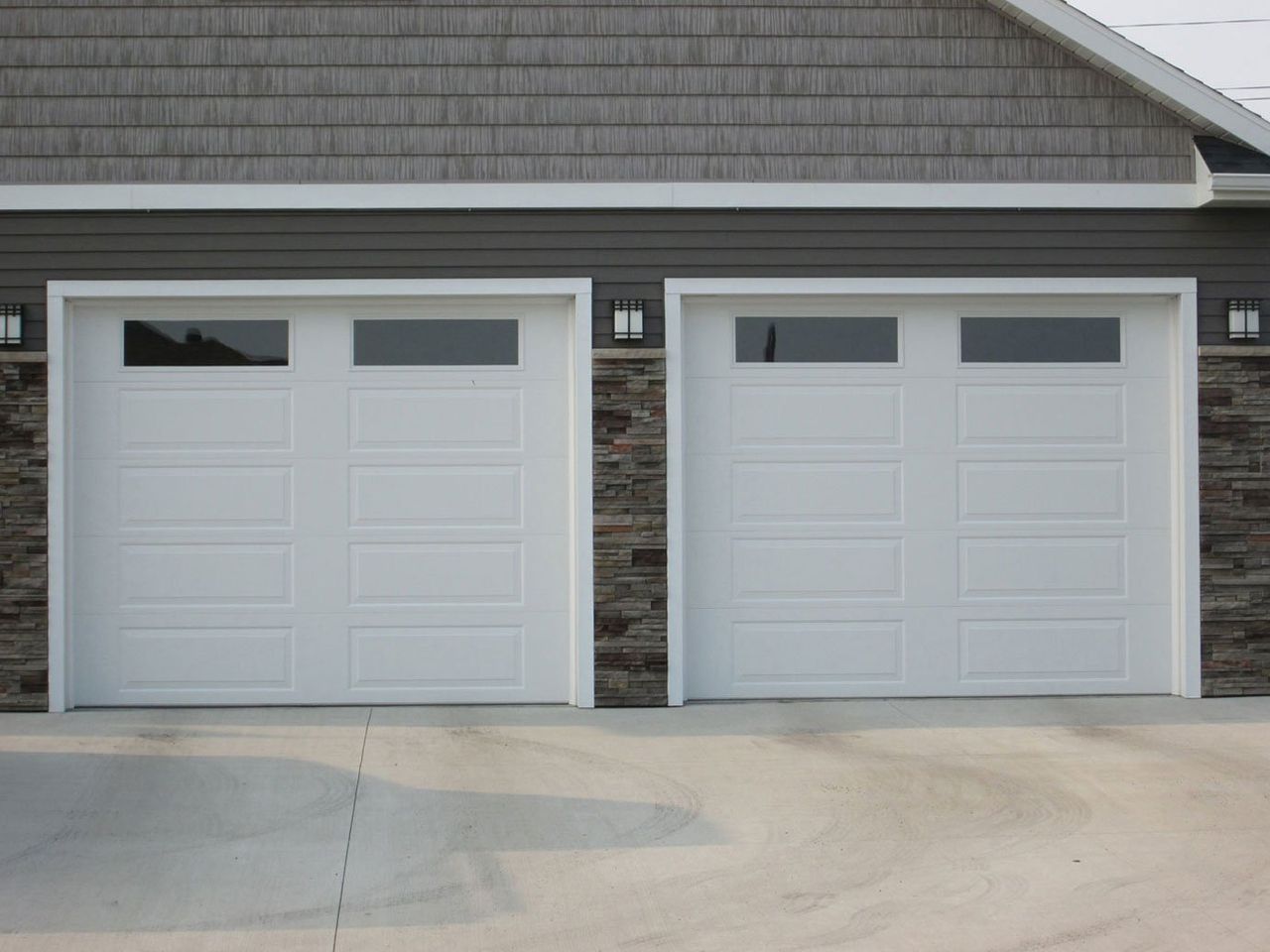 Two white garage doors on a suburban house with a concrete driveway
