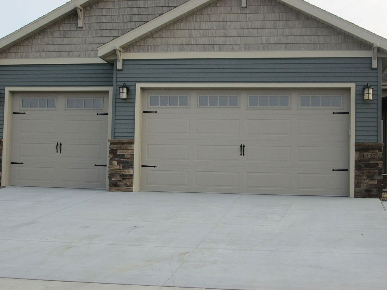 Two gray garage doors on a blue house with stone trim and a concrete driveway
