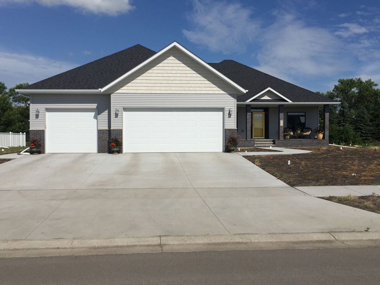 Suburban house with a three-car garage and wide concrete driveway under a blue sky