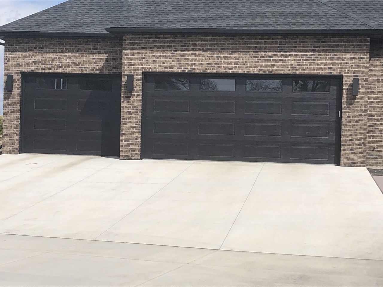 Brick house with two black garage doors and a wide concrete driveway