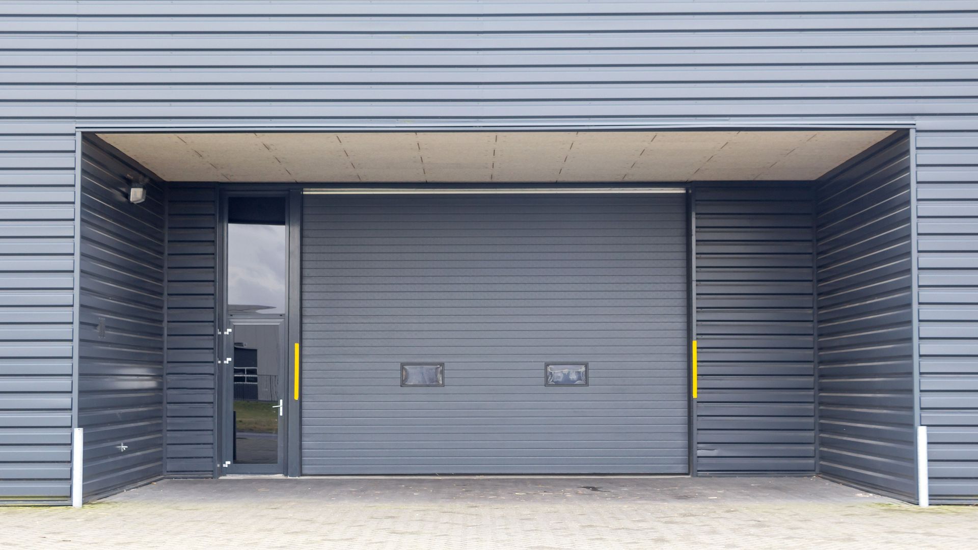 Modern gray loading dock with a closed roll-up door and side entry door under a covered overhang