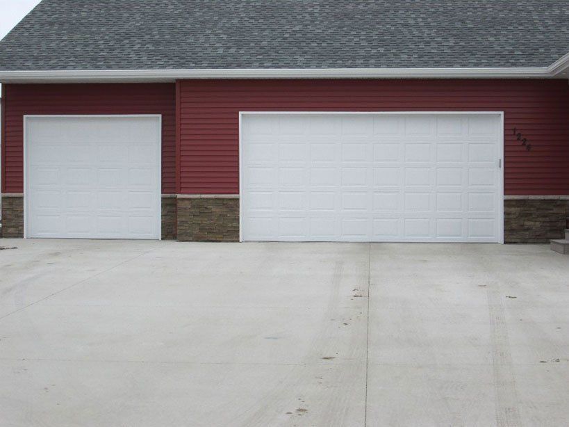 Two white garage doors on a red house with a wide concrete driveway