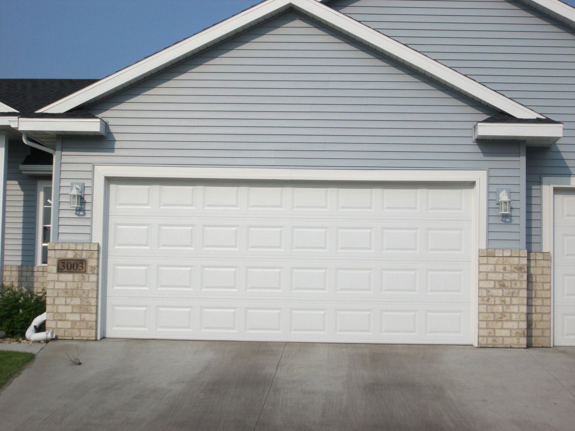 Gray suburban house with a white double garage door and stone pillars by the driveway