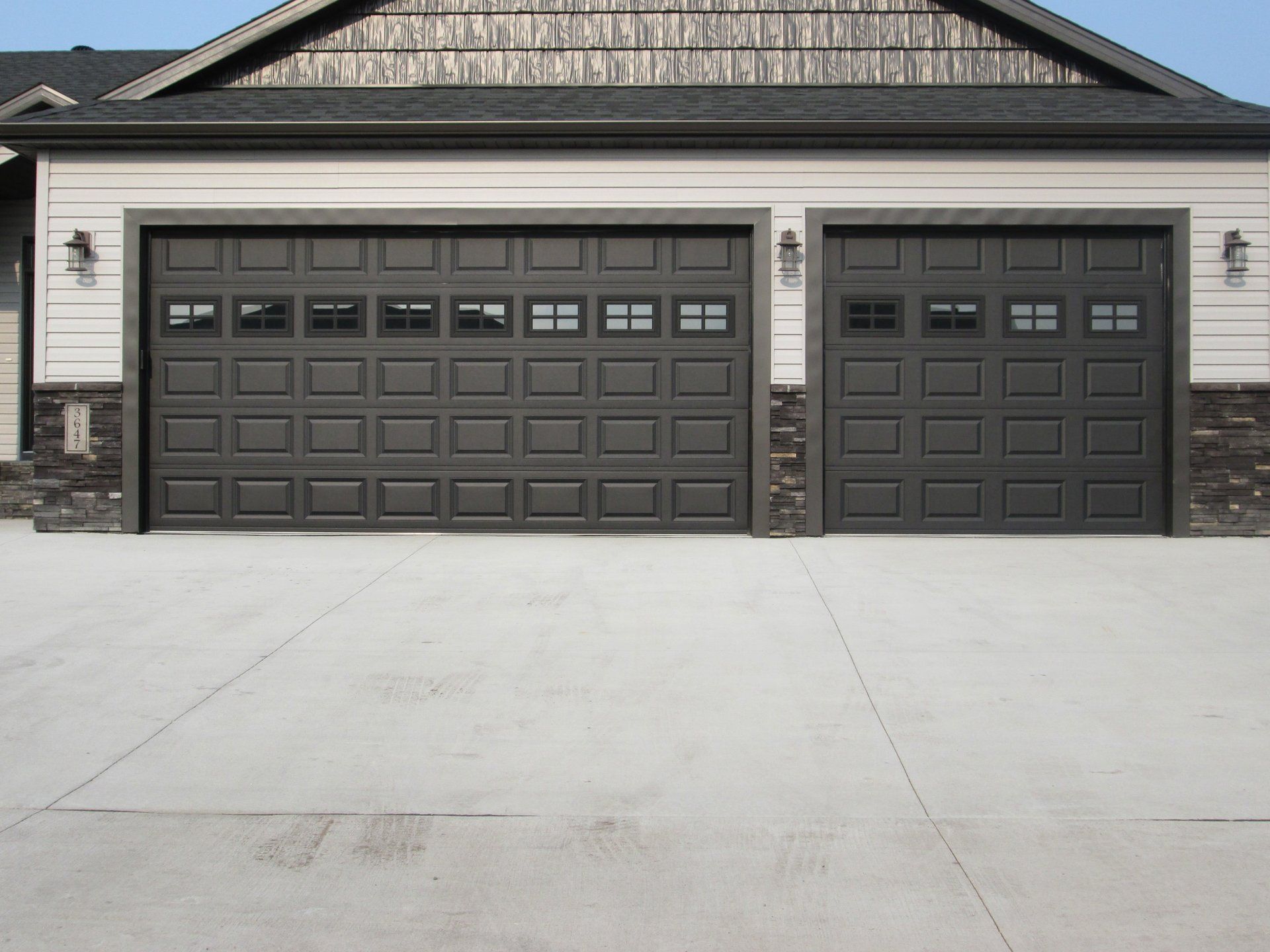 Two dark gray garage doors on a house with a large concrete driveway.