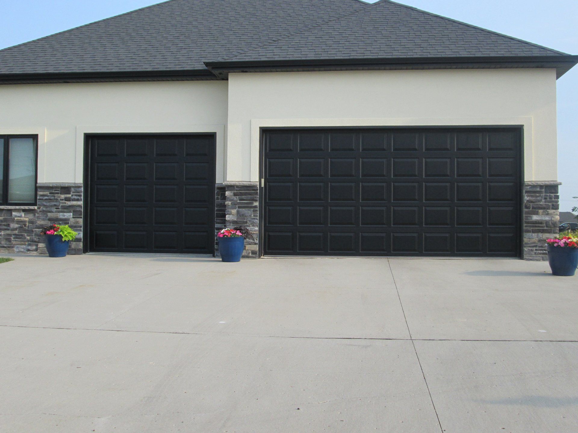 Modern house exterior with two black garage doors and flower pots on a concrete driveway