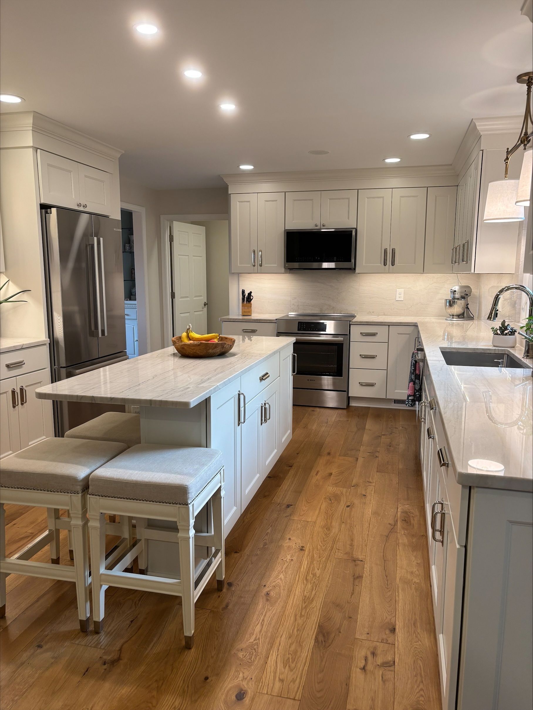 A kitchen with white cabinets , stainless steel appliances , hardwood floors and a large island.