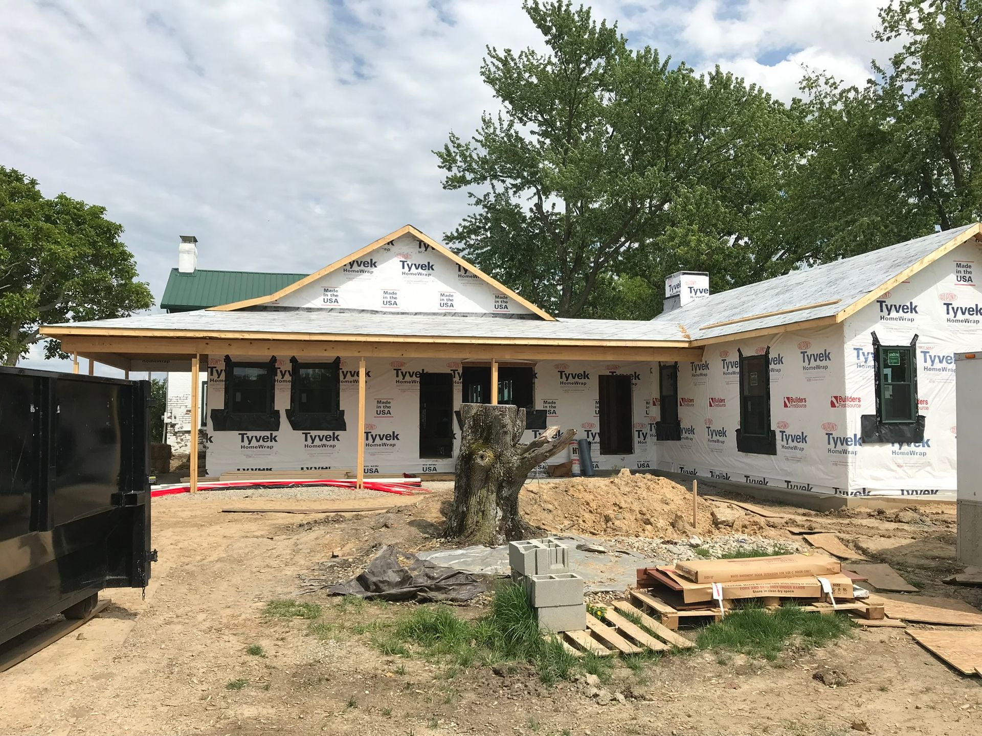 Partially constructed white house with green trim, porch, and scattered building materials in a yard