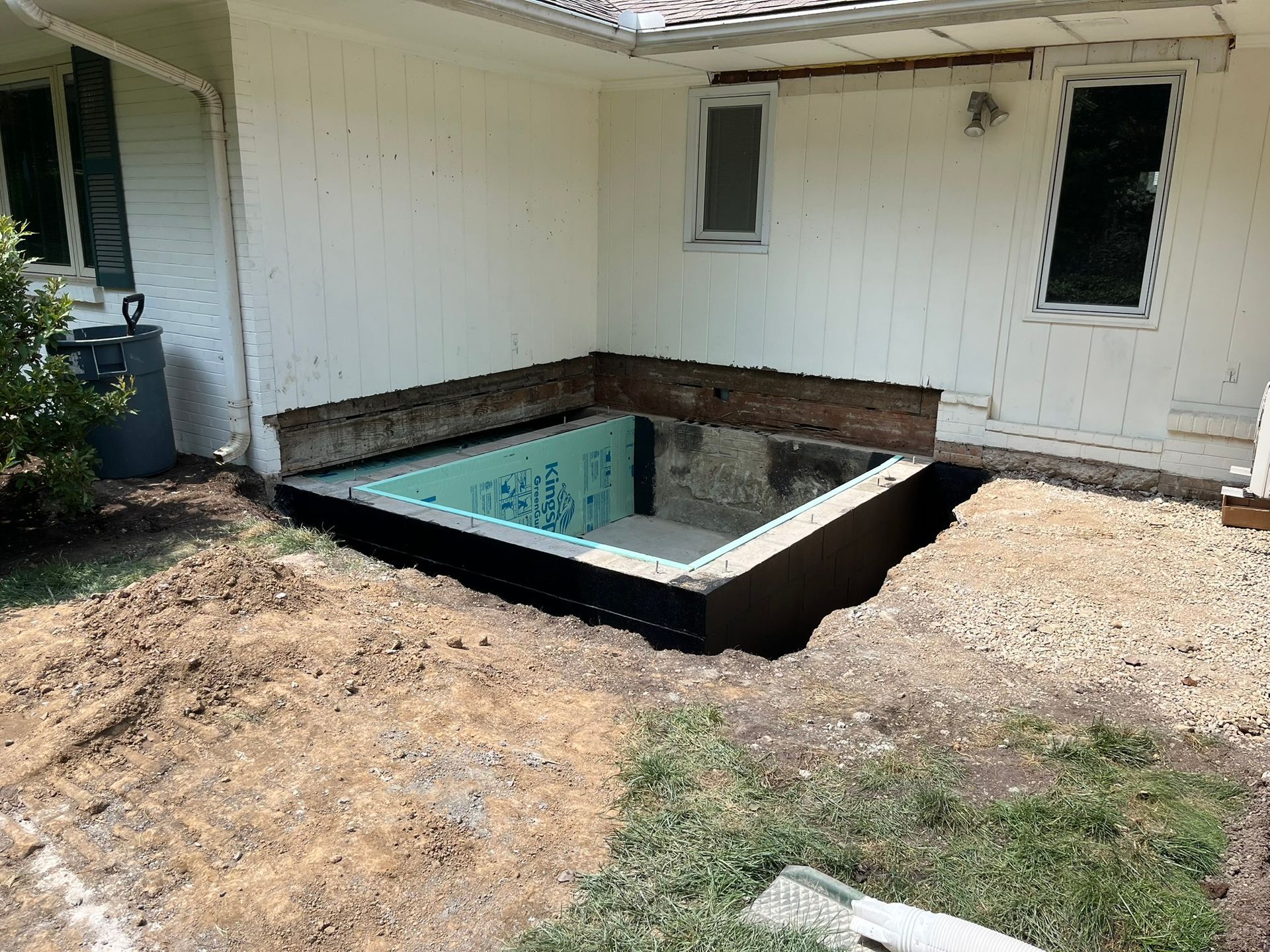 Small backyard with an empty square in-ground pool beside a house and gravel ground