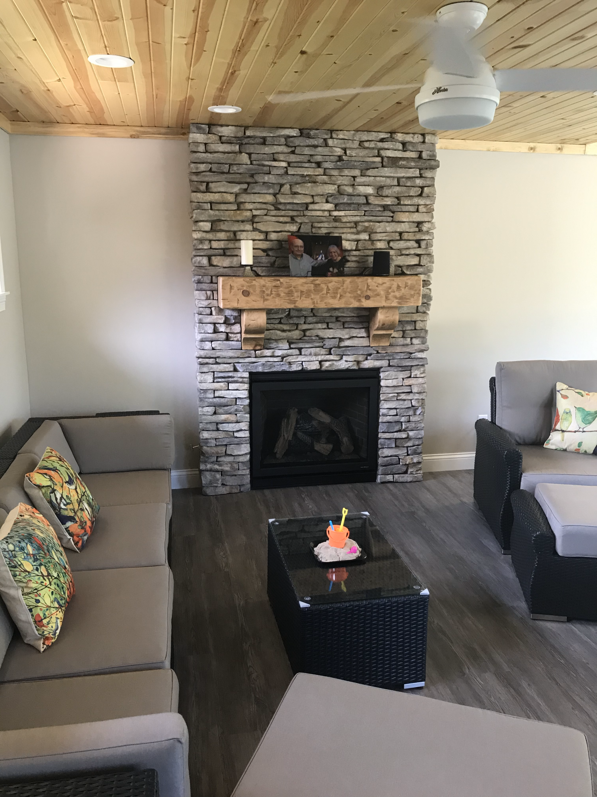 A living room with a stone fireplace and a ceiling fan