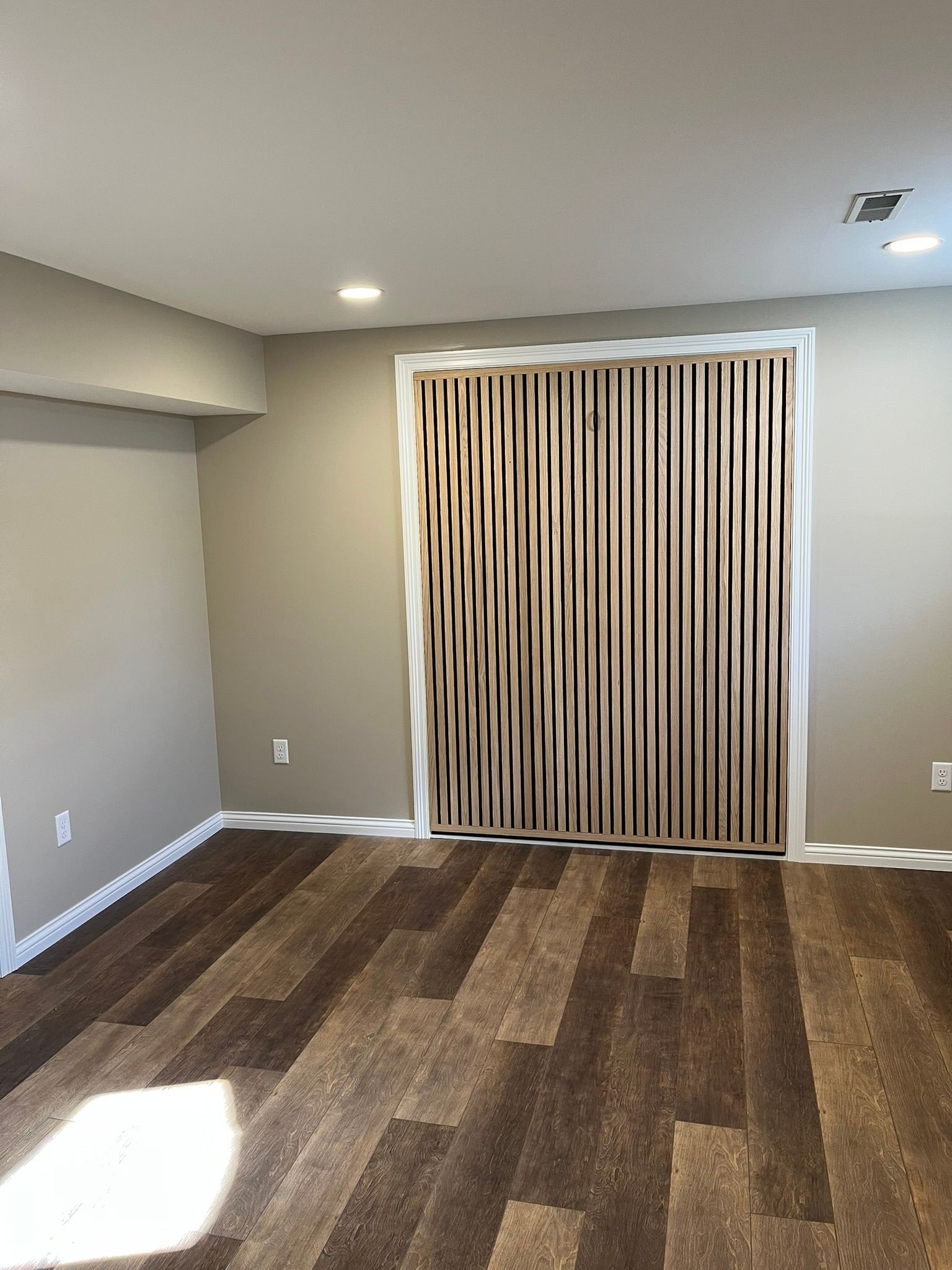 Empty beige room with wood-look flooring and vertical blinds covering a sliding glass door.