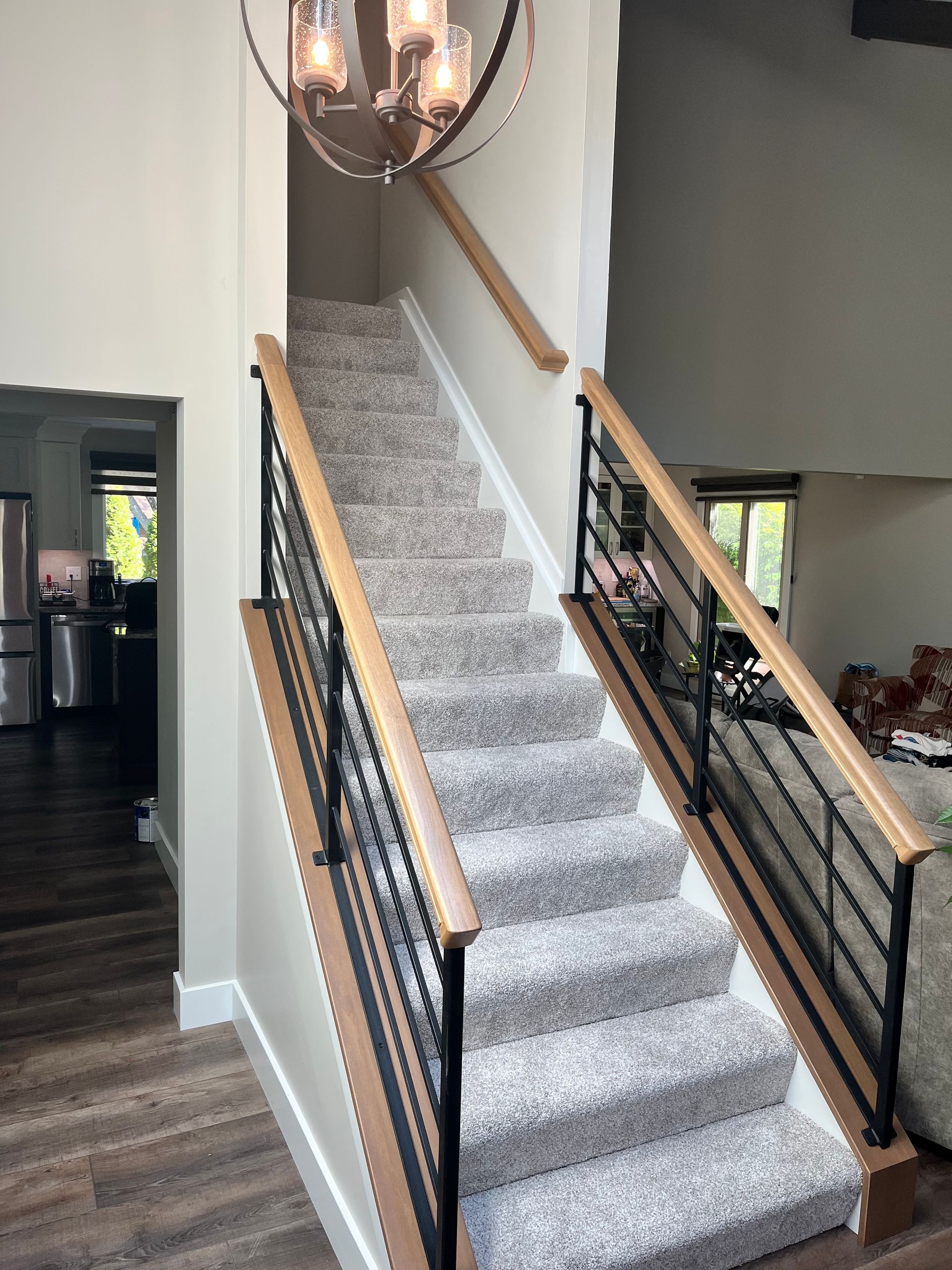 Carpeted staircase with black metal railings and a chandelier in a modern home interior
