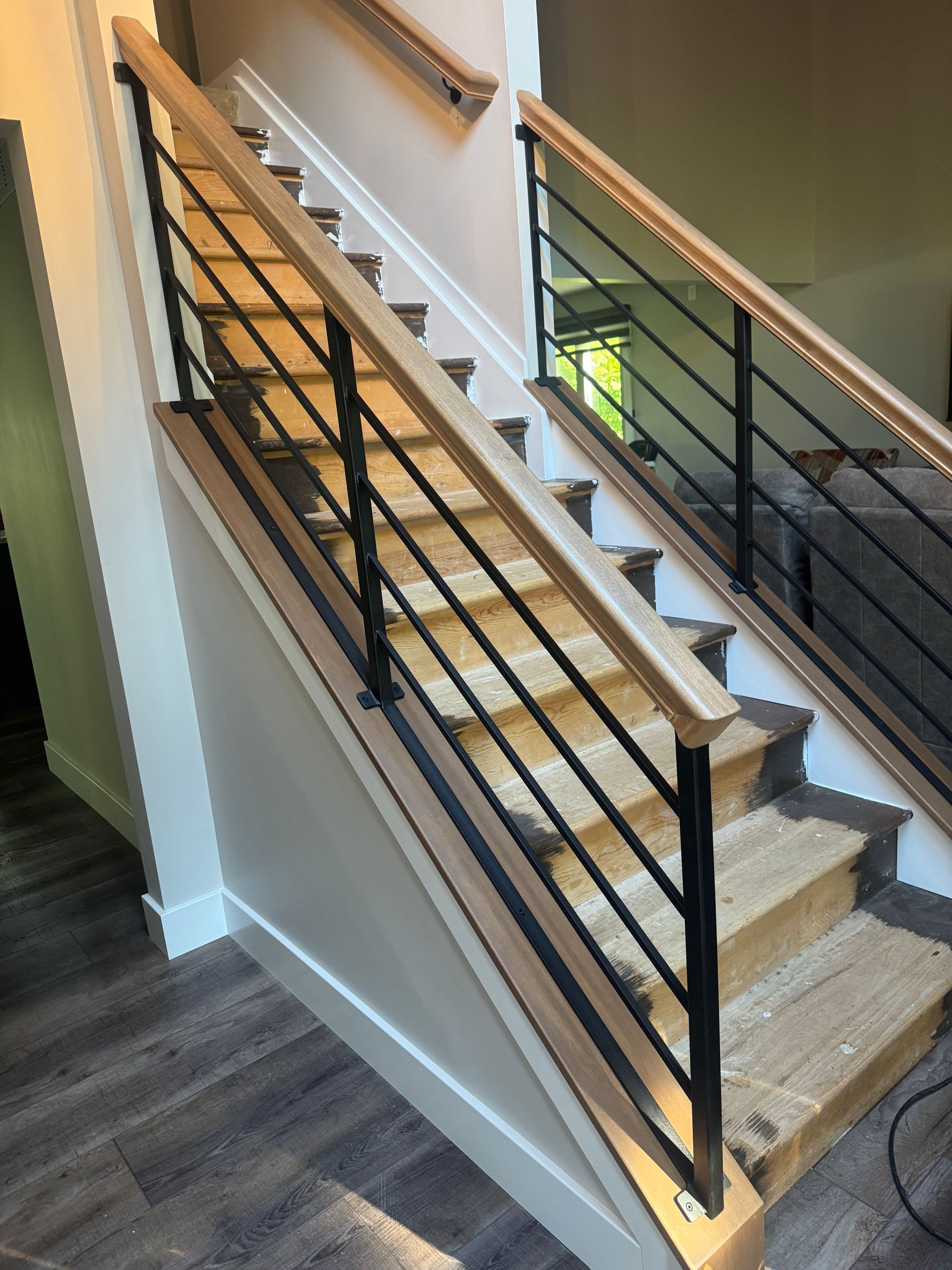 Indoor staircase with wood steps, black railings, and white walls, lit by daylight.
