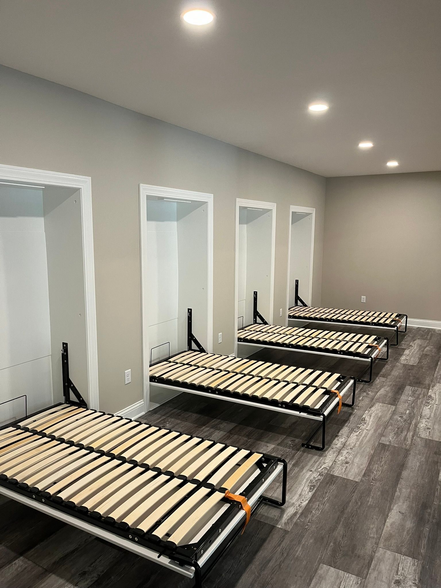 Row of adjustable hospital beds in a bright empty recovery room with gray walls and wood flooring