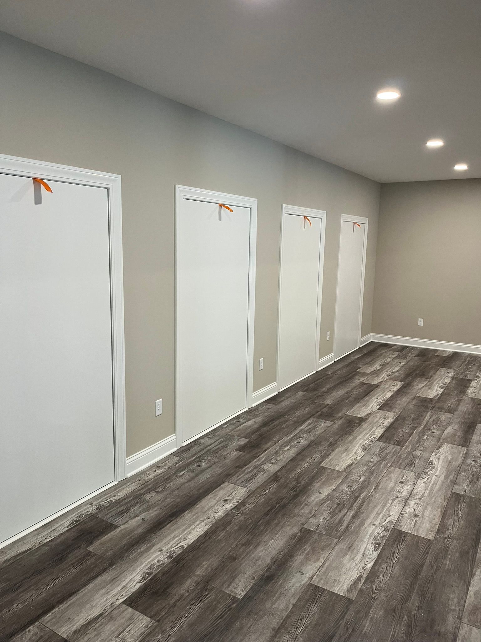 Empty hallway with white doors, gray walls, and wood-patterned flooring