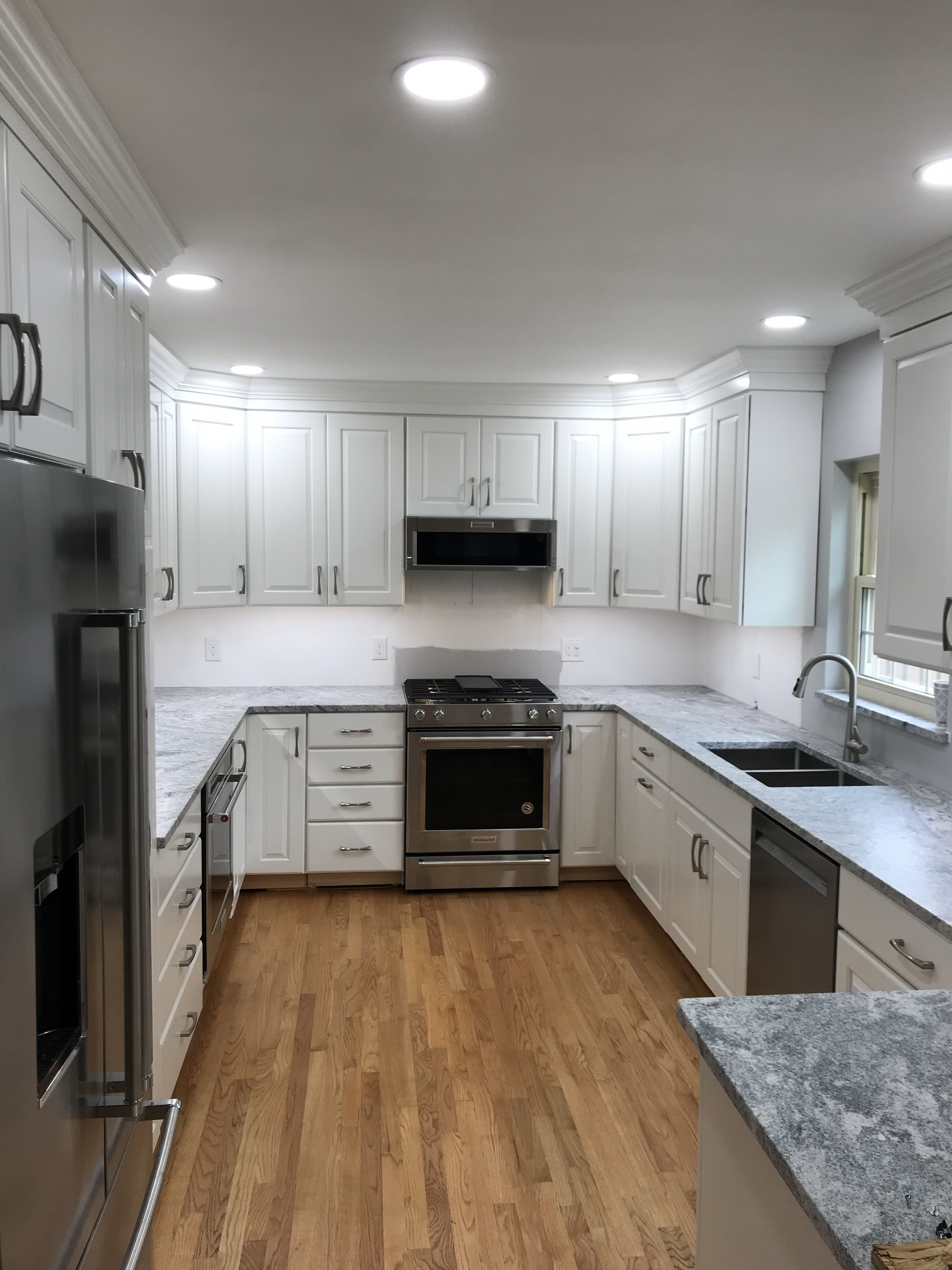 A kitchen with white cabinets , stainless steel appliances , granite counter tops and hardwood floors.