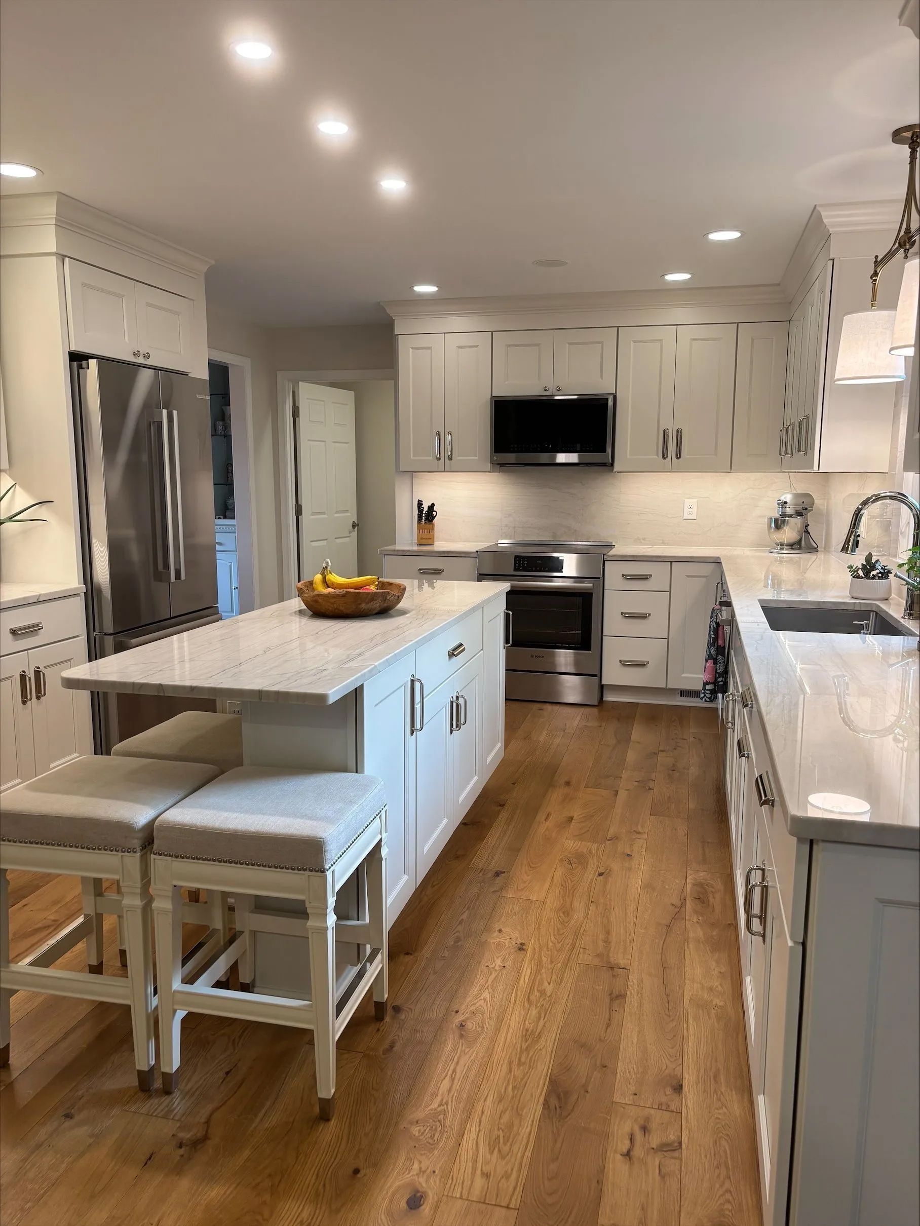 A kitchen with white cabinets, stainless steel appliances, hardwood floors and a large island.