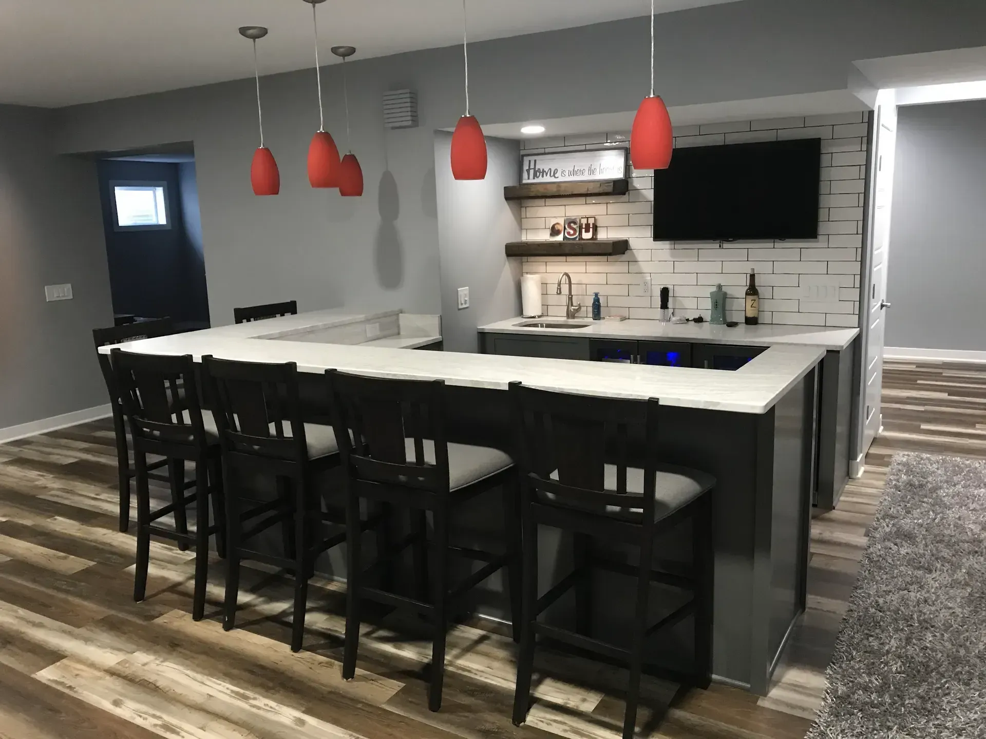 A kitchen with a bar and stools and a flat screen tv.