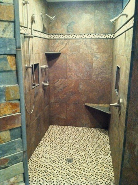A walk in shower with a tiled floor and a stone wall