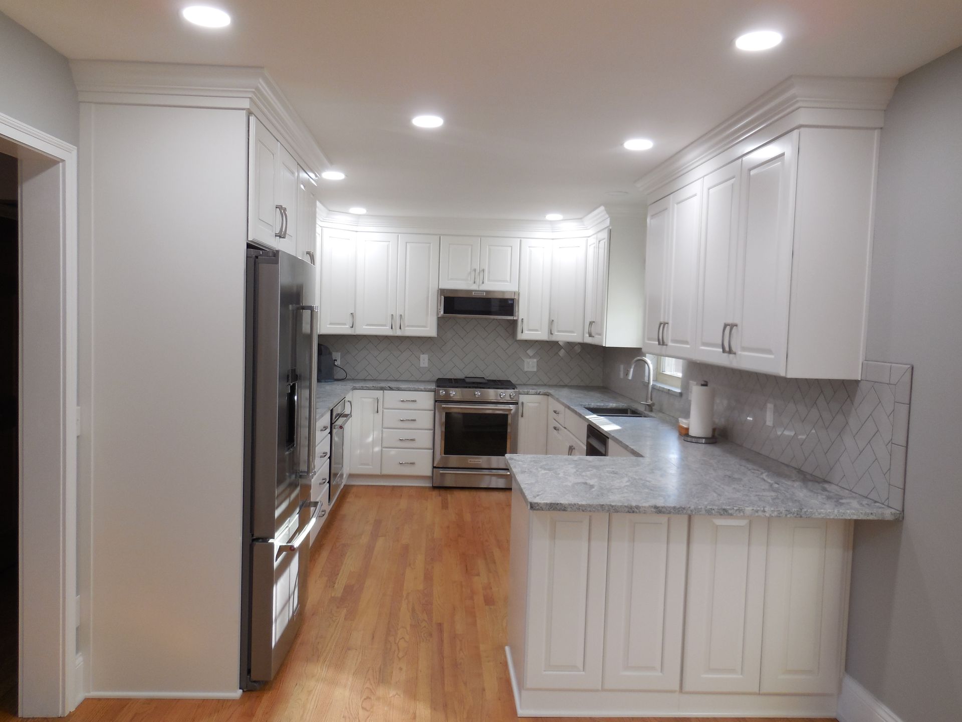 White kitchen with granite countertops, stainless steel appliances, and wood flooring.