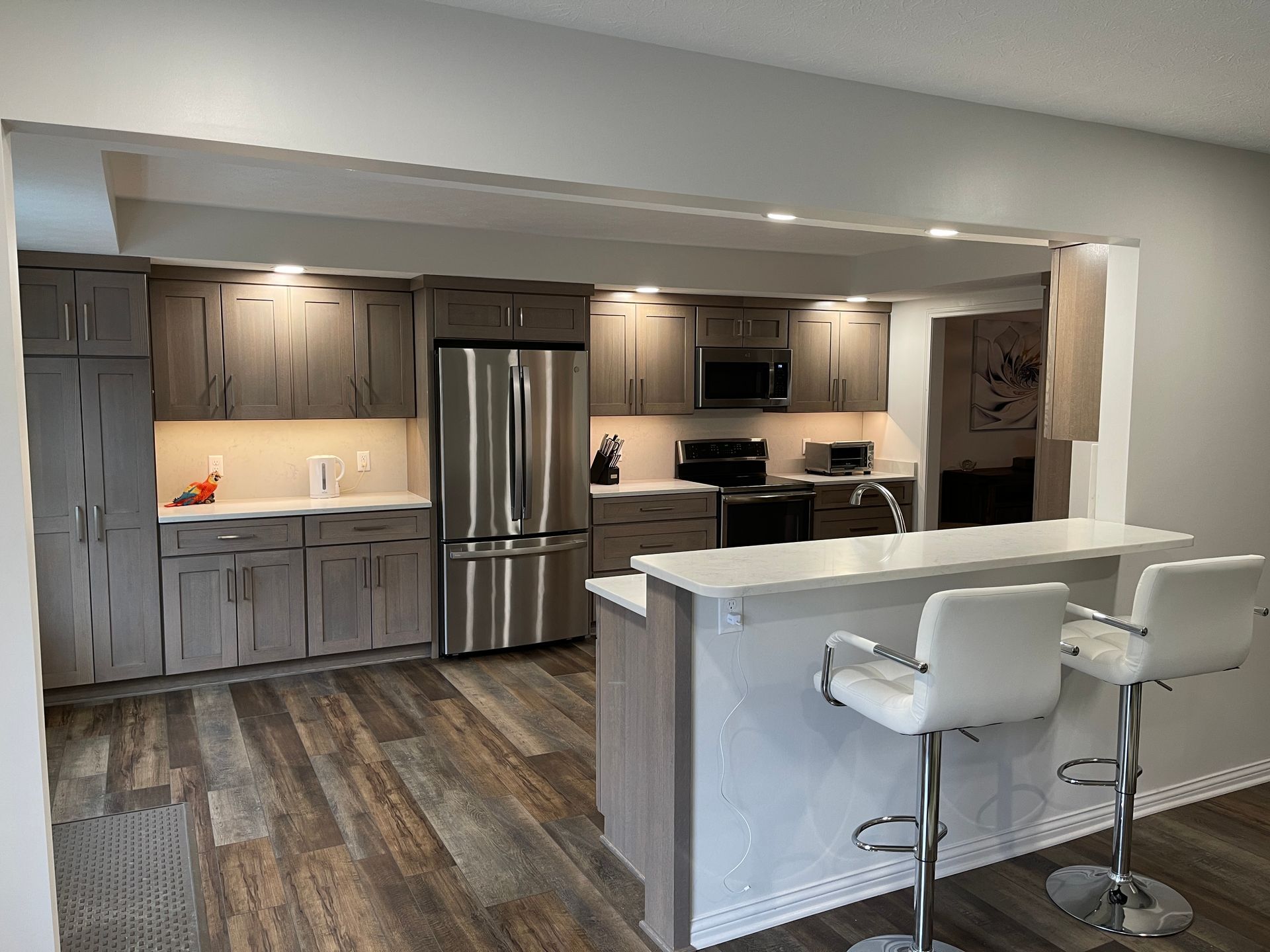 Modern kitchen with gray cabinets, stainless steel appliances, and a breakfast bar with white stools.
