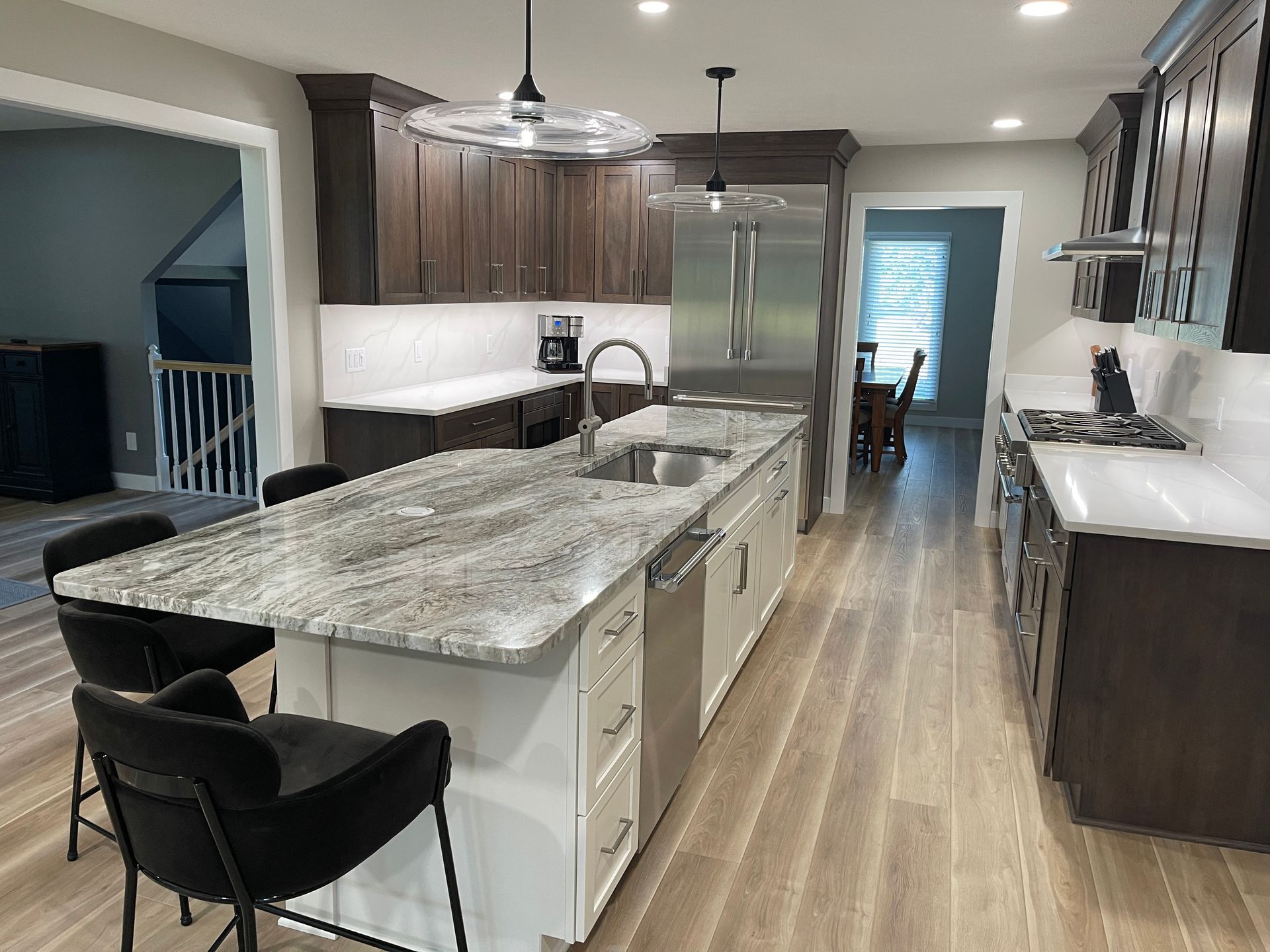 Modern kitchen with granite island, dark wood cabinets, stainless steel appliances, and light wood flooring.