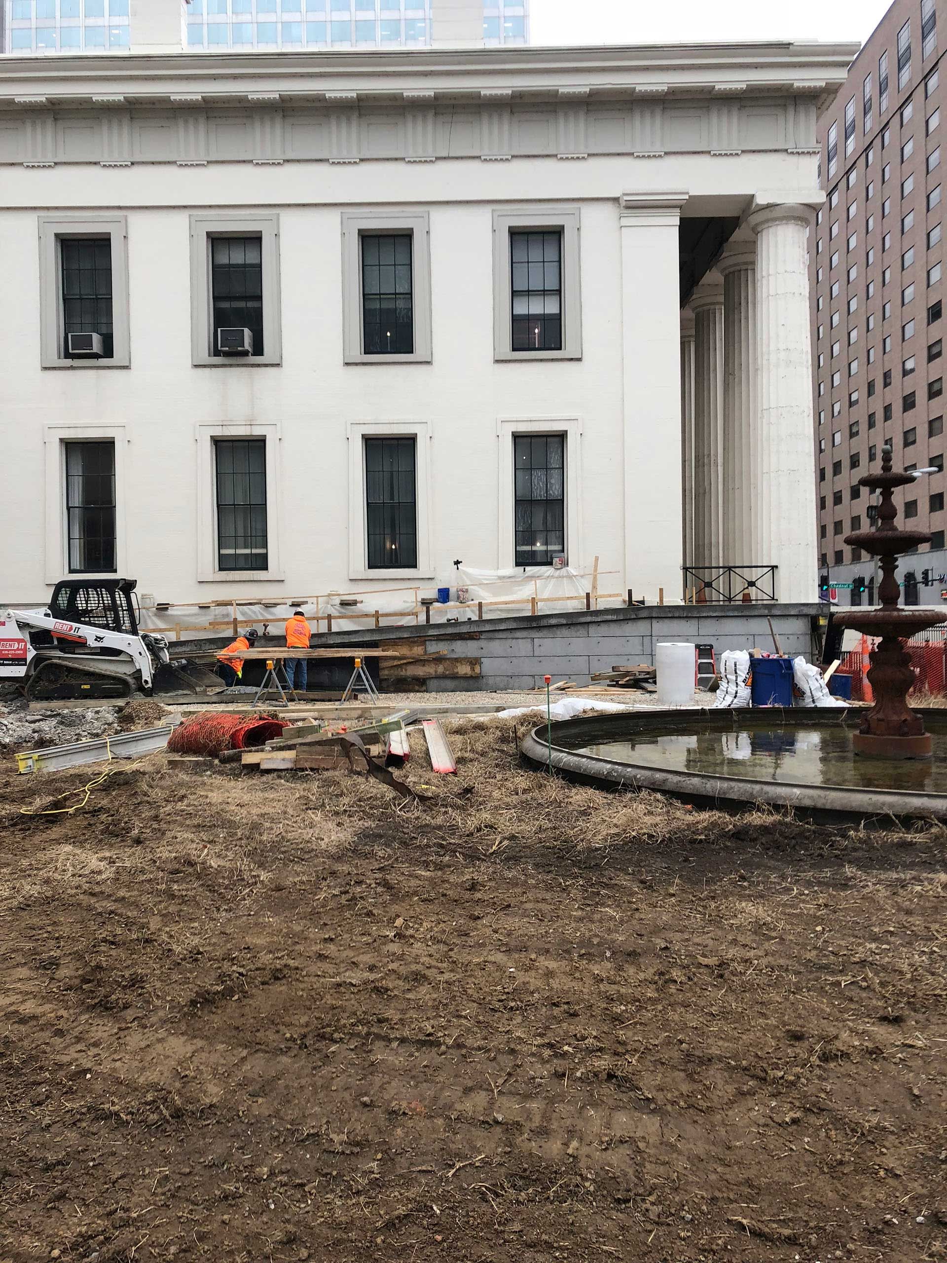 Construction site in front of a white neoclassical building with excavated dirt and workers nearby