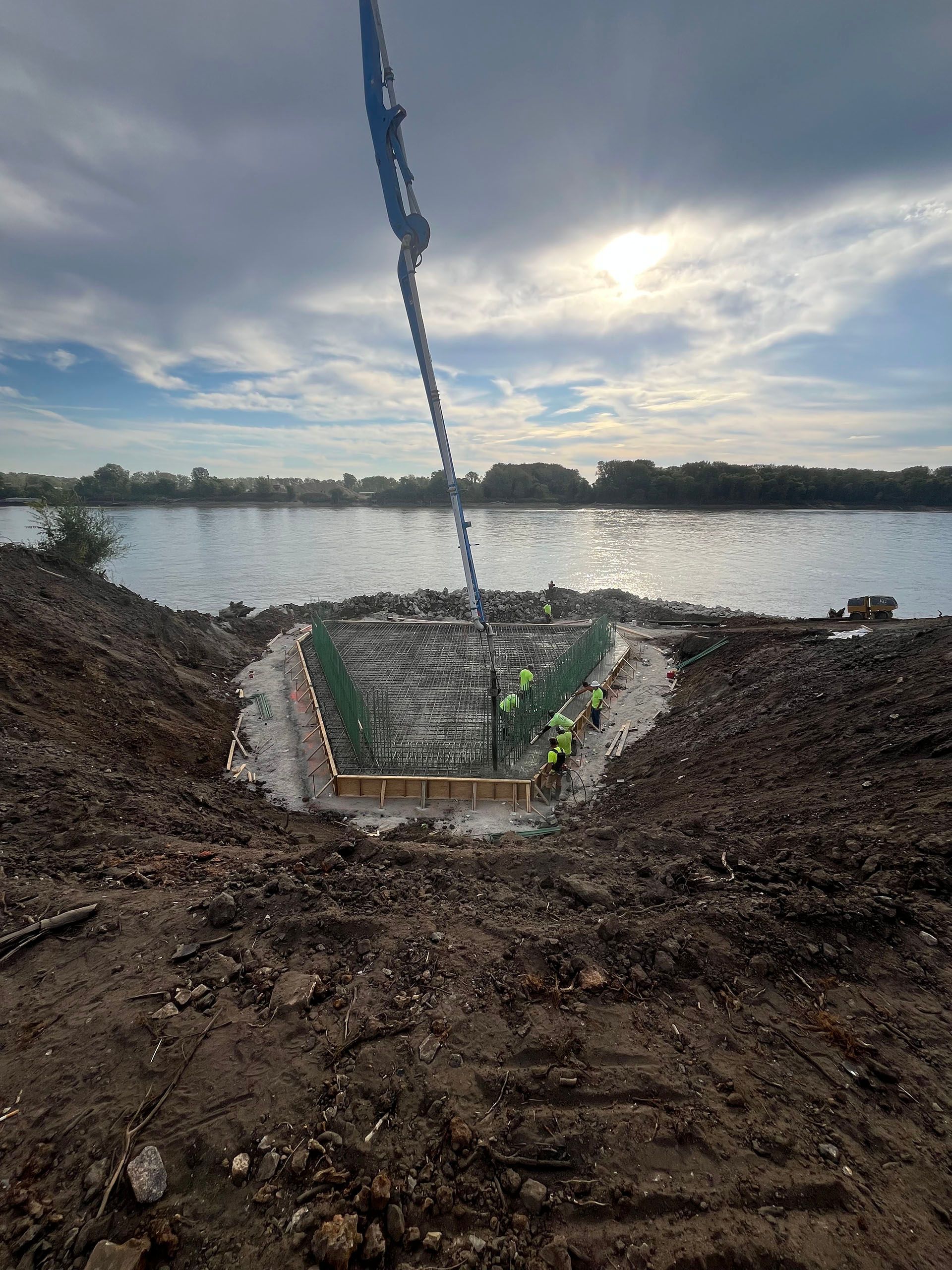 Excavation trench leading to a calm river at sunset, with muddy banks and cloudy sky