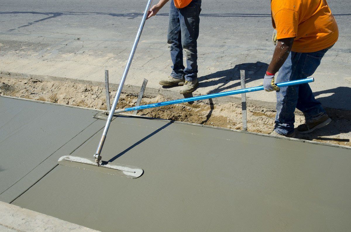Workers smoothing wet concrete with tools on a sidewalk construction site