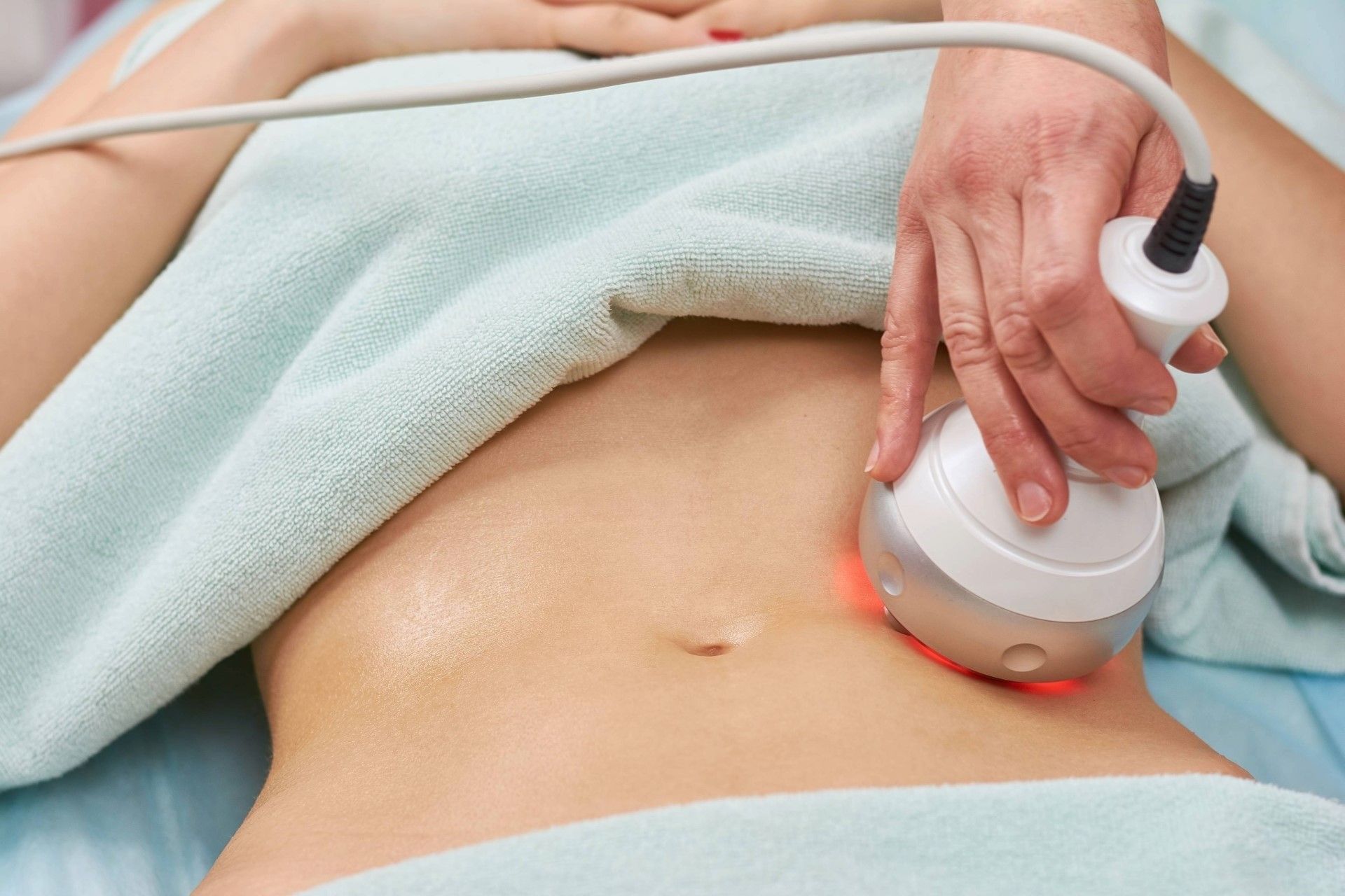 Person receiving body contouring treatment on abdomen with device emitting red light.