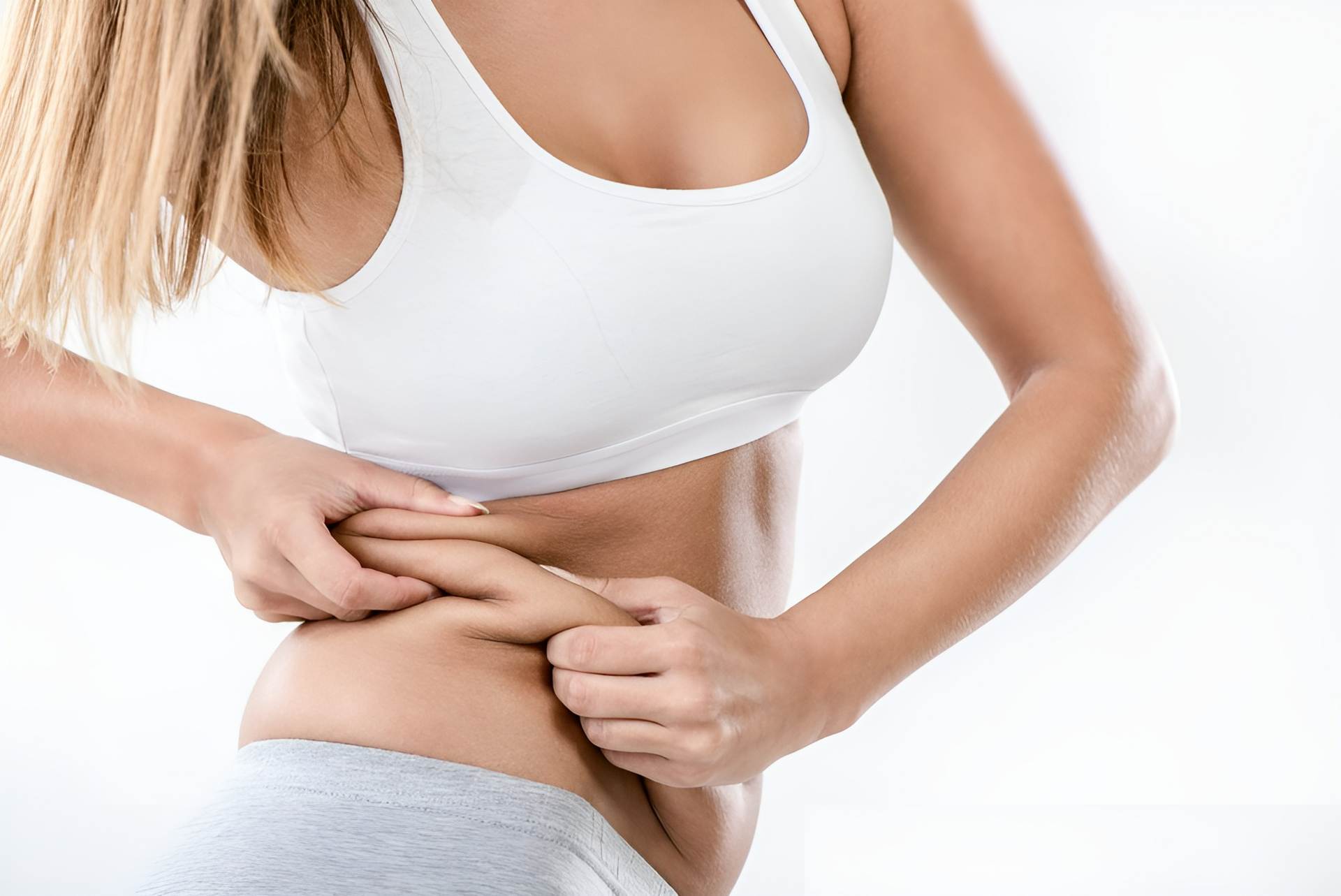Woman in white top and gray shorts pinching stomach fat.