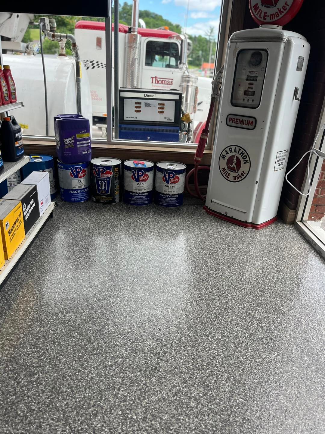 A gas pump is sitting on the floor of a gas station next to a window
