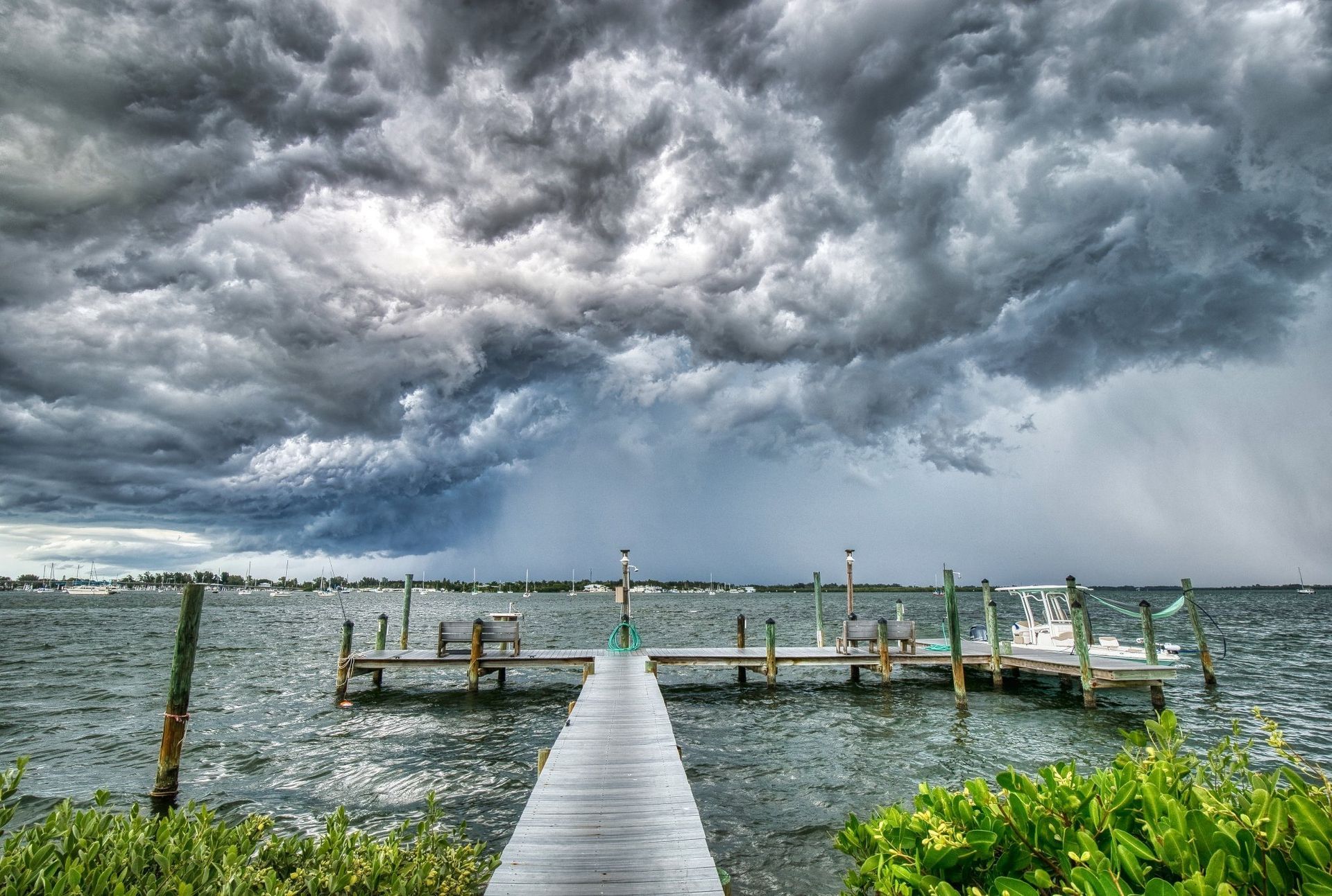 A wooden dock extends into a choppy bay under a dramatic, dark, storm-filled sky with rain falling in the distance.